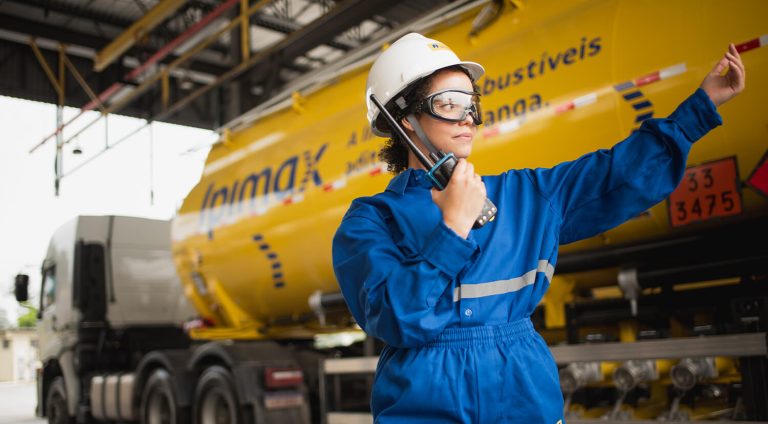 mulher com epis de seguranca do trabalho ajudando manobrar um caminhão da ipimax em um Galpão