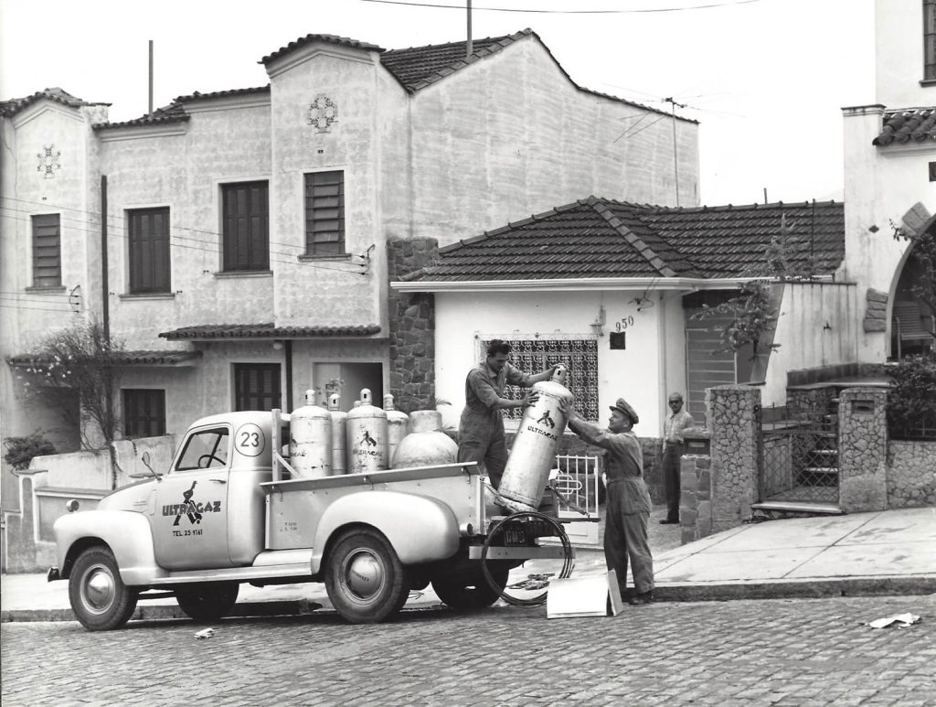 Dois colaboradores da Ultragaz, da década de 40, descarregando um botijão de gás na casa de um cliente.