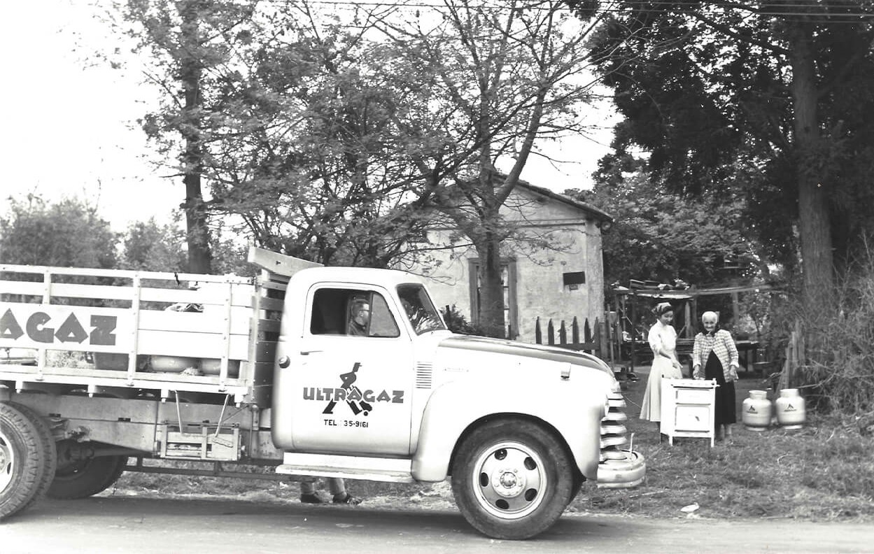 Caminhão de entregas de botijões da Ultragaz realizando a descarga do produto para duas clientes.