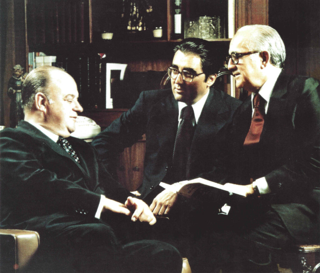 Três executivos do Grupo Ultra em reunião nos anos 1980, sentados em escritório com estante ao fundo, conversando sobre documentos
